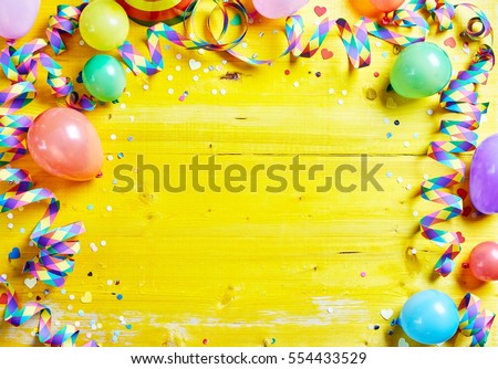 Bright colorful carnival or party frame of balloons, streamers and confetti on a rustic yellow wood table with central copy space for your greeting , invitation or advertising