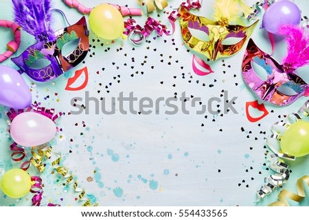 Fun carnival, masquerade or Mardi Gras frame with bright metallic masks with feathers above red lips on a light blue textured background with copy space, streamers and confetti