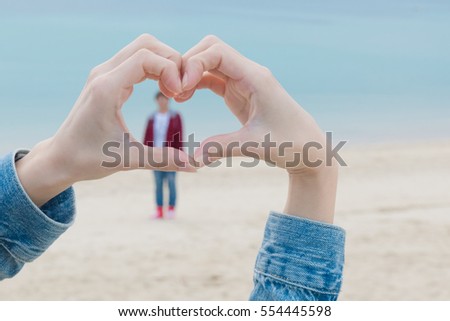 Close up of heart made by female hands background the turquoise ocean