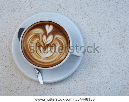 A white porcelain cup of hot latte with triple hearts  latte art on the polished stone top table