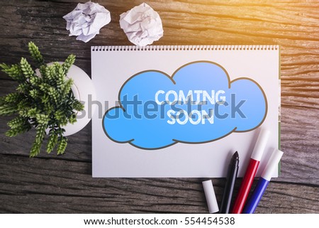 COMING SOON word with Notepad and green plant on wooden background