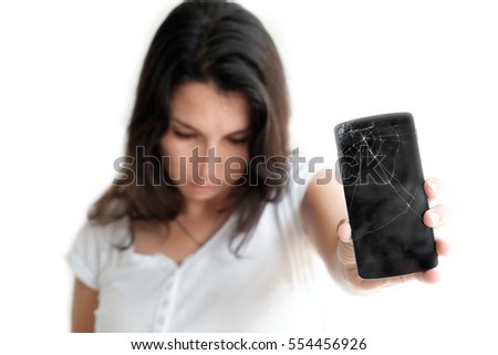 Young woman  emotionally reacts on broken phone. Pretty woman holding crashed mobile phone in her hand. Selective focus on broken display of cracked smartphone. Isolated on white background