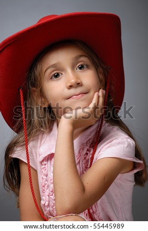 Close up of a little girl wearing a cowboy hat holding her chin up smiling