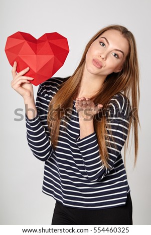 Beautiful woman holding red polygonal paper heart shape blowing a kiss at camera