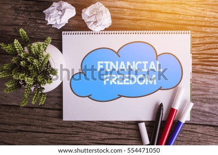 FINANCIAL FREEDOM word with Notepad and green plant on wooden background