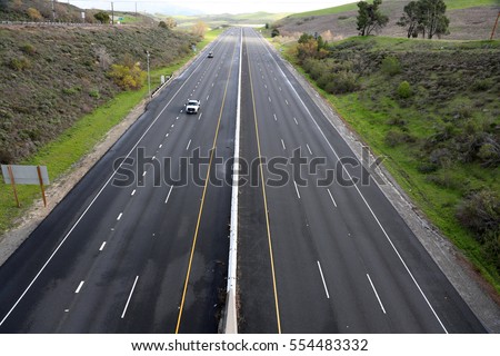 a beautiful 6 lane highway on a toll road in Orange County California with cars and green valley walls on both sides Royalty-Free Stock Photo #554483332