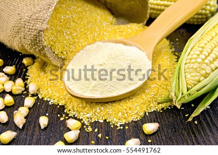 Flour corn in a spoon, cereal in sackcloth and on the table, the cob on the background dark wooden boards Royalty-Free Stock Photo #554491762