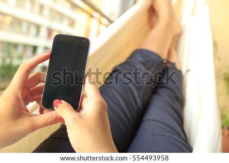 Woman resting in a hammock with a smartphone with the screen off, in black. Ideal image for mock up.