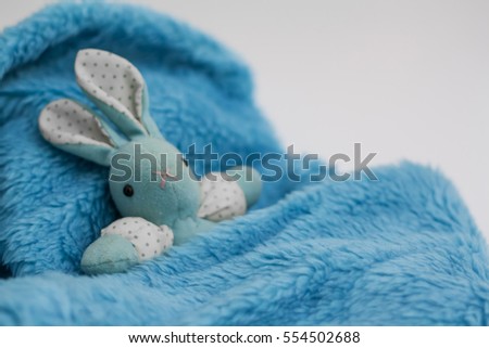 Bunny doll plush lying in fluffy soft bed, old blue rabbit toy with dotted sleeves and ears. Baby sleeping concept. Burred photo, selective focus on mouth.