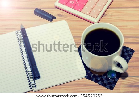 Open notebook and a cup of coffee on wooden background.