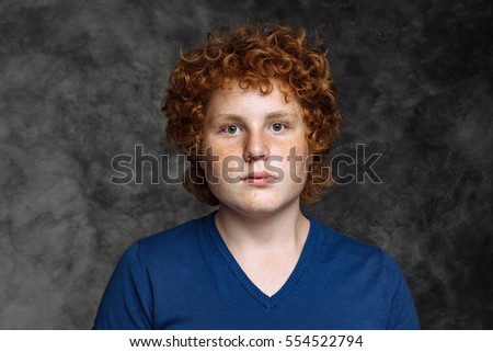 Studio portrait of curly red-haired freckled teenager in blue shirt