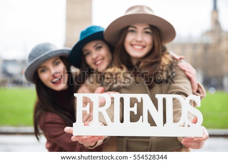 Portrait of three happy female students holding sign friends in London 