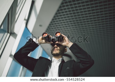 Businessman with binoculars spying on competitors. Royalty-Free Stock Photo #554528524