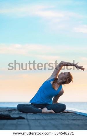 Beautiful woman practicing yoga on the pier at sunrise