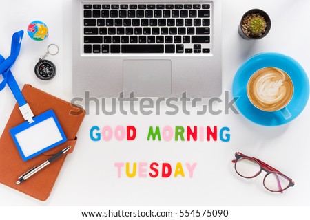 Caption word  Good morning tuesday. White office desk with laptop, diary, eyeglasses, compass, pen, blank identification card and cup of coffee on white background.