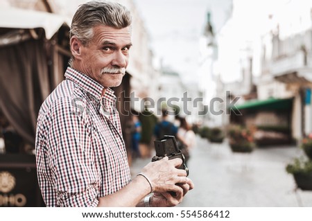 Confident photographer. Handsome mature man holding retro style camera while standing on the street.