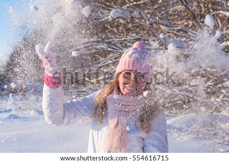 Winter snow fight happy girl throwing snow playing outside. Joyous young white woman having fun in nature forest park on snowy day wearing pink outerwear with warm accessories: gloves, hat, scarf.