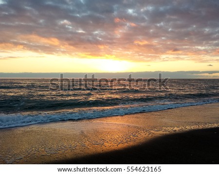 Golden lights of the winter sunset are reflected on sea waves and sandy beach 