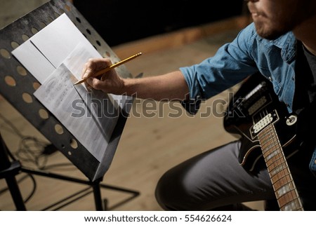 people, art and entertainment concept - man with guitar writing notes to music book at studio Royalty-Free Stock Photo #554626624