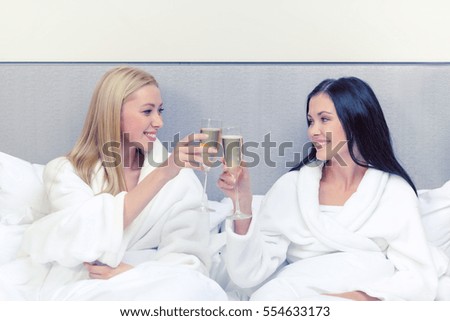 hotel, travel, friendship and happiness concept - smiling girlfriends with champagne glasses in bed