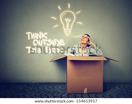 Think outside the box concept. Young woman coming out of box with great bright idea light bulb isolated on gray wall background 