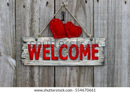 Red welcome sign hanging by rope on antique rustic wood door with red country hearts and black house key; Valentine's Day background