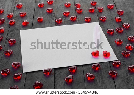 Red hearts made of glass on wooden background. White sheet of paper as a free space for text.