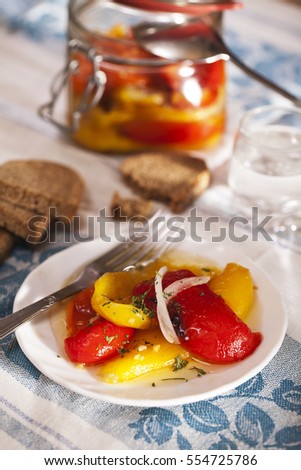 Bell peppers grilled in a marinade. On blue tablecloth white plate with peppers, fork and bread, can with homemade pickled peppers.
