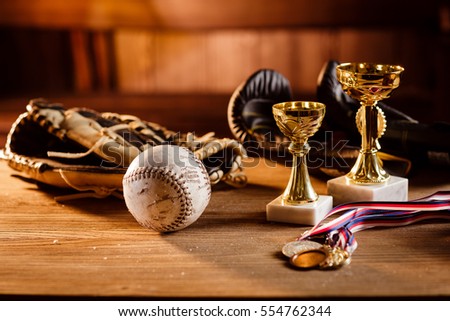Still life of trophy, medals, vintage boxing gloves,  grunge baseball gloves with white ball over wooden table and dark background, with warm shiny lights in front of wooden background. Royalty-Free Stock Photo #554762344