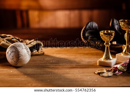Still life of trophy, medals, vintage boxing gloves,  grunge baseball gloves with white ball over wooden table and dark background, with warm shiny lights in front of wooden background. Royalty-Free Stock Photo #554762356
