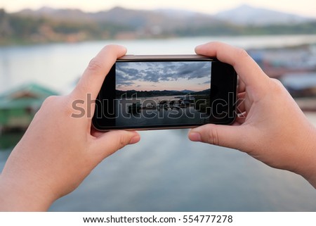 Hands of travelers using mobile landscape photography at dawn on the river in Sangkhlaburi, Kanchanaburi, Thailand