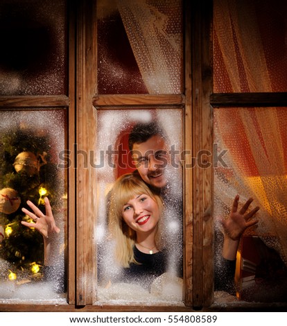happy cheerful man and woman looking through the frozen window