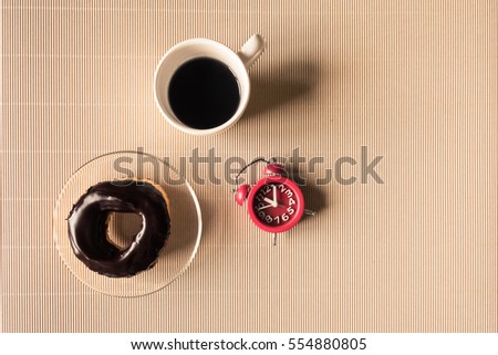 Top view of coffee cup with donut and clock on table.