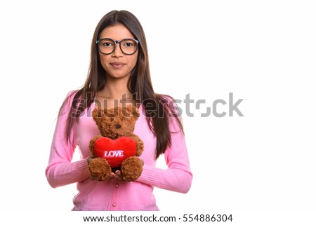 Studio shot of young beautiful Brazilian nerd woman holding teddy bear with heart and love sign isolated against white background
