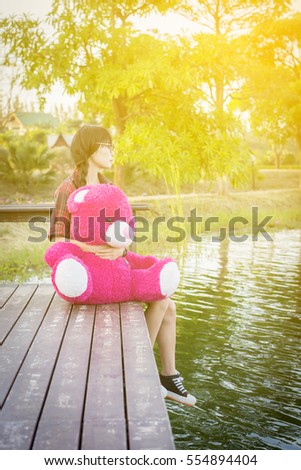 Happy woman sitting hugging a teddy bear on the bench by the pool. Vintage tone.