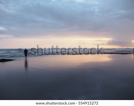 A man walking along the black sand beach during sunset in Bali