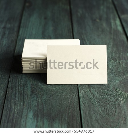 A photo of a blank white thick cardboard business card next to a pile of them, on a dark wooden background texture. A square mockup or a minimalist banner with copyspace