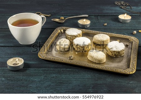 A photo of mantecados and polvorones, traditional Spanish cookies, on a vintage tray with a cup of tea and candles on a dark wooden background