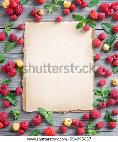 Open recipe book with fresh raspberries and mint leaf on wooden background. Copy space, top view, high resolution product.