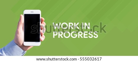 Smart phone in hand front of green background and written WORK IN PROGRESS