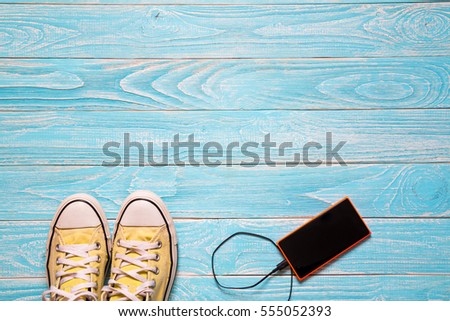 Couple youth sneakers, yellow and white sneakers, shoes and mobile on blue wooden floor, footwear close-up, shoes for youth, sports shoes. Valentine's Day. Concept of sport, healthy lifestyle.