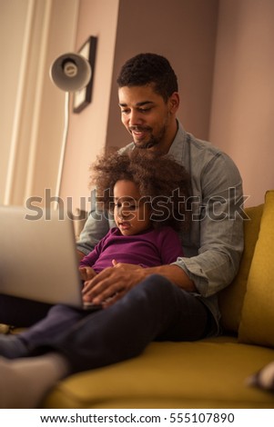 Cute african american dad and daughter using laptop at home.