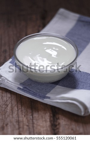 white yogurt in small glass bowl on cotton cloth place on old wood background. 