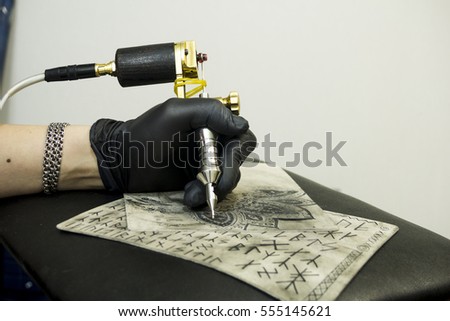 Hand of tattoo artist holding tattoo machine in process of tattooing training skin. Black gloves, concentration, art process