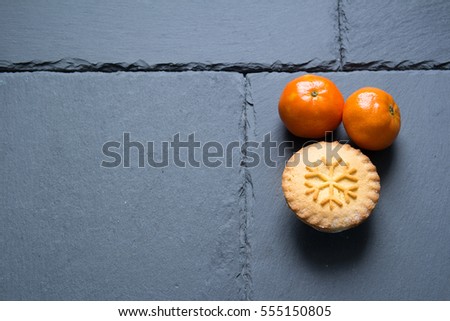 This is a simple picture of two tangerines and a Christmas Mince Pies on a grey, slate, background. Slate placemat. Slate table. Space for text. Break time with friends.