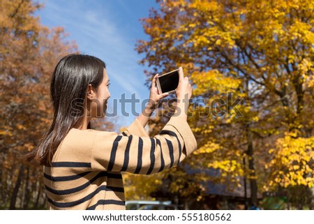 Woman taking photo by cellphone in autumn season