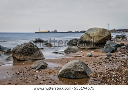 Seascape with stones and boats at the pier in the background.