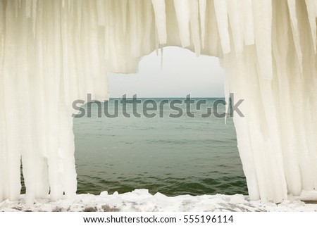 View of the sea through an arch from icicles on a moody icy day after winter storm
