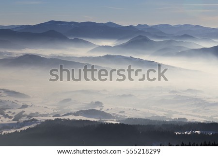 Winter mountain landscape -  top view of  snow, mist covered valley in the background of mountain peaks. Ski resort Kubinska Hola; Western Tatras. Travel destination for winter vacations and skiing.