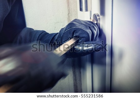 masked burglar with crowbar breaking and entering into a victim's home - shot with dramatic motion Royalty-Free Stock Photo #555231586